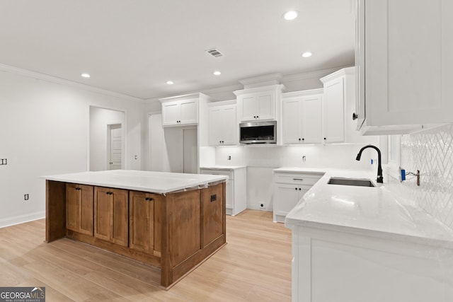 kitchen featuring tasteful backsplash, a sink, light wood finished floors, stainless steel microwave, and crown molding