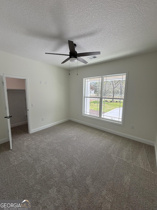 carpeted empty room with visible vents, ceiling fan, a textured ceiling, and baseboards