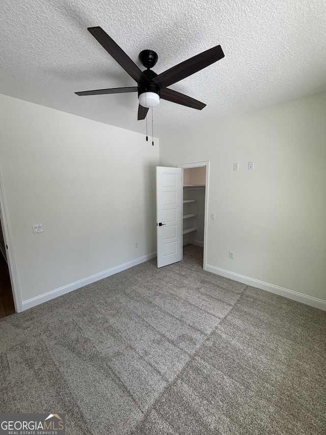 unfurnished bedroom with a ceiling fan, a textured ceiling, carpet flooring, baseboards, and a spacious closet