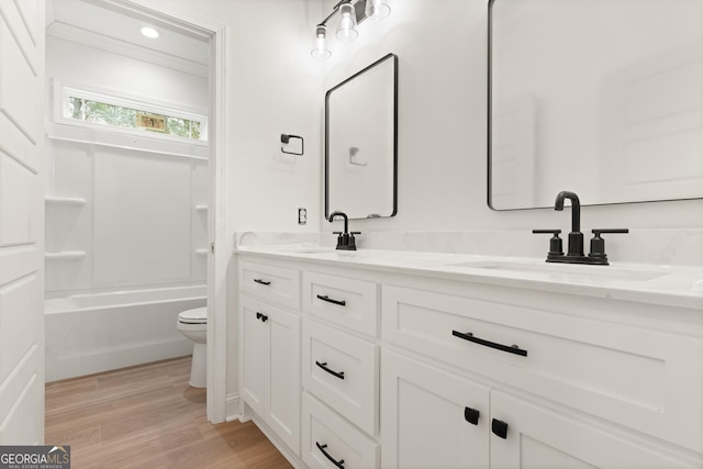 bathroom with double vanity, a sink, toilet, and wood finished floors