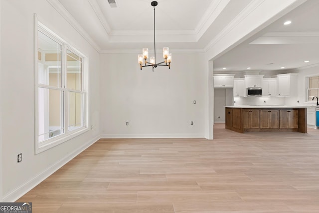 unfurnished dining area with light wood-style floors, a raised ceiling, crown molding, and an inviting chandelier