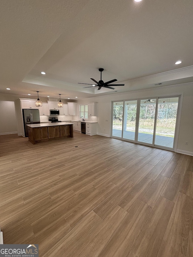 unfurnished living room with a wealth of natural light, recessed lighting, light wood-style floors, and a tray ceiling