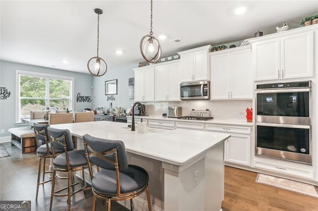 kitchen with white cabinetry, a kitchen island with sink, pendant lighting, and appliances with stainless steel finishes