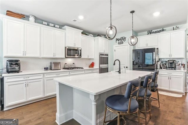 kitchen with dark hardwood / wood-style flooring, stainless steel appliances, sink, a center island with sink, and white cabinetry