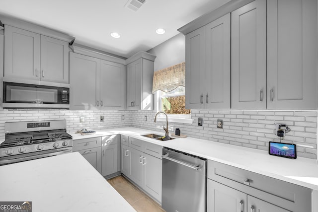 kitchen with light tile patterned floors, gray cabinets, stainless steel appliances, tasteful backsplash, and sink