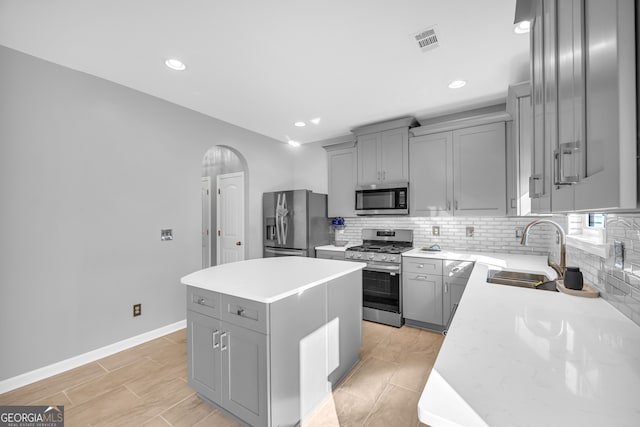 kitchen with stainless steel appliances, gray cabinetry, backsplash, a center island, and sink