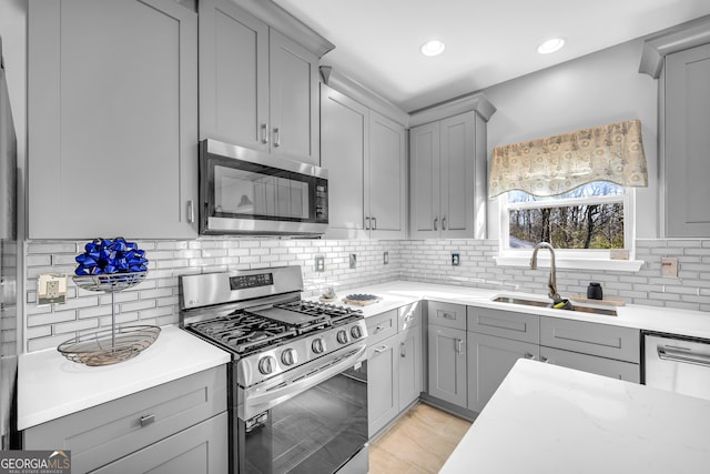 kitchen with gray cabinets, stainless steel appliances, decorative backsplash, and sink