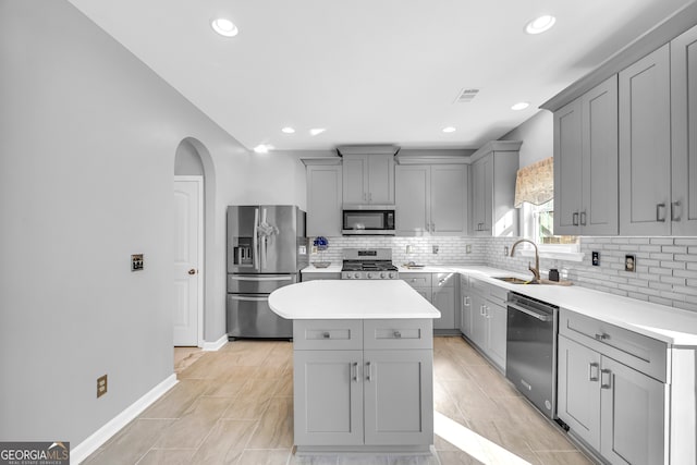 kitchen with appliances with stainless steel finishes, a center island, decorative backsplash, sink, and gray cabinets