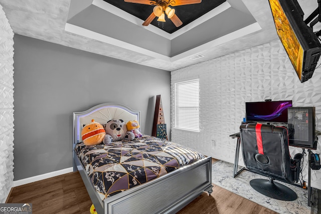 bedroom with ceiling fan, hardwood / wood-style floors, and a raised ceiling