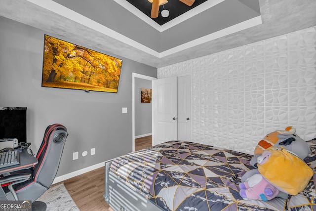 bedroom with ceiling fan, a raised ceiling, and hardwood / wood-style floors