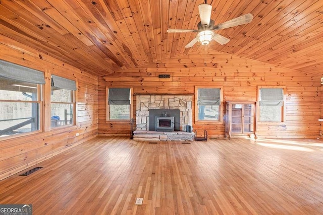 unfurnished living room featuring a wood stove, wood walls, hardwood / wood-style floors, vaulted ceiling, and wood ceiling