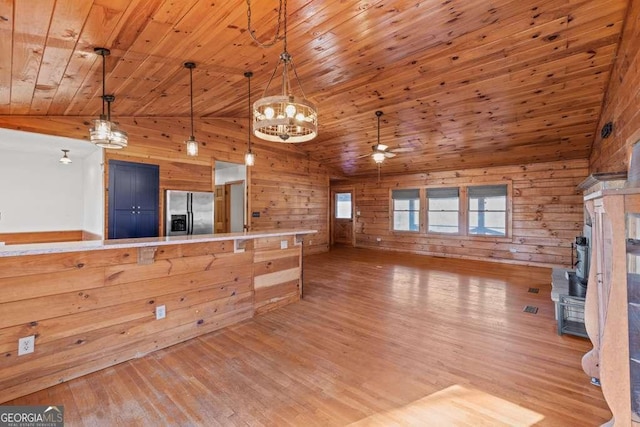 kitchen with light wood-type flooring, ceiling fan with notable chandelier, decorative light fixtures, stainless steel fridge with ice dispenser, and wood walls