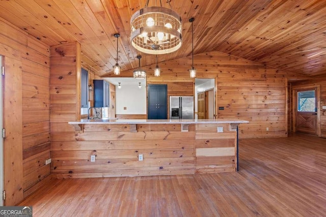 kitchen with decorative light fixtures, kitchen peninsula, stainless steel refrigerator with ice dispenser, and wooden walls