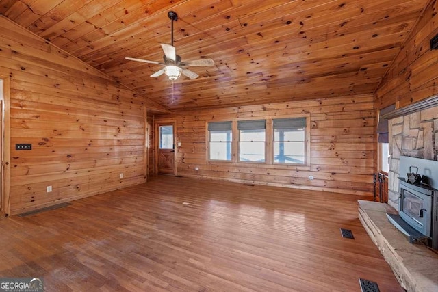 unfurnished living room with plenty of natural light, a wood stove, wood ceiling, and vaulted ceiling