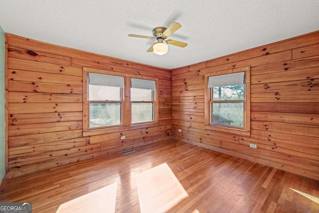 unfurnished room with ceiling fan, wood-type flooring, a textured ceiling, and wooden walls