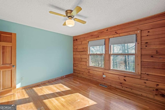 empty room featuring a textured ceiling, light wood-type flooring, ceiling fan, and wood walls