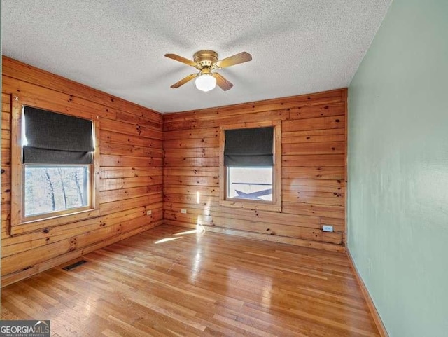 spare room with light hardwood / wood-style floors, ceiling fan, and wooden walls