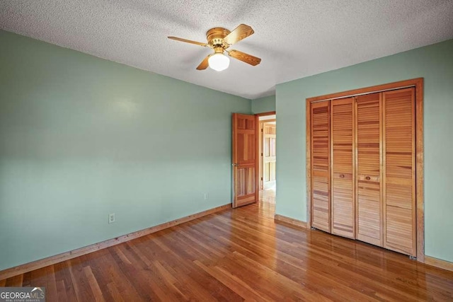 unfurnished bedroom with ceiling fan, a closet, wood-type flooring, and a textured ceiling