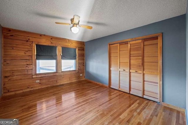 unfurnished bedroom with a textured ceiling, ceiling fan, wooden walls, light hardwood / wood-style floors, and a closet