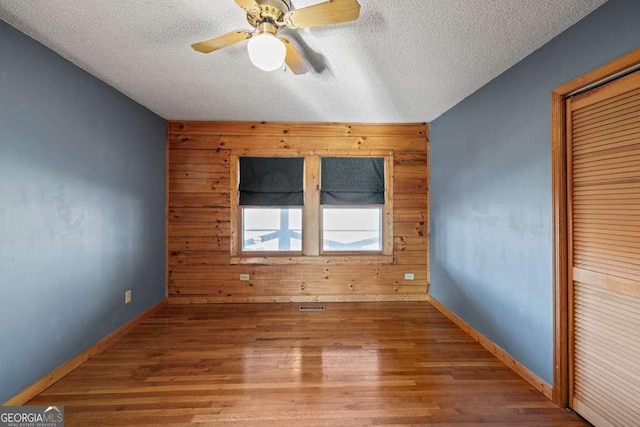 spare room with hardwood / wood-style flooring, ceiling fan, wood walls, and a textured ceiling