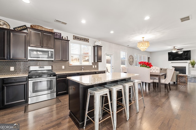 kitchen featuring a breakfast bar, stainless steel appliances, a center island, dark hardwood / wood-style floors, and hanging light fixtures