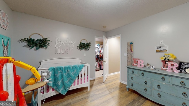 bedroom with a textured ceiling, hardwood / wood-style flooring, and a nursery area