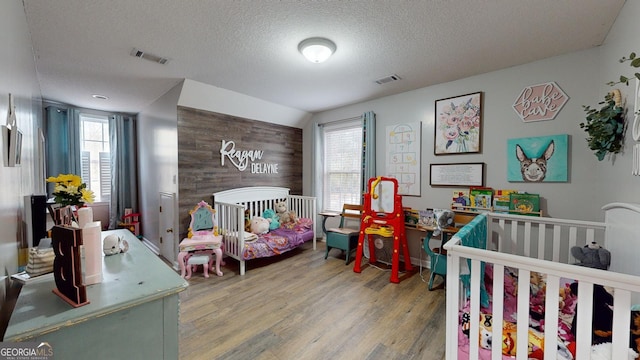 bedroom featuring a crib, multiple windows, a textured ceiling, and hardwood / wood-style flooring