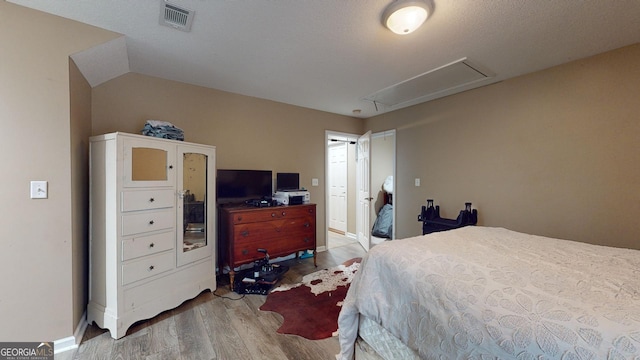 bedroom with hardwood / wood-style flooring, a textured ceiling, and vaulted ceiling