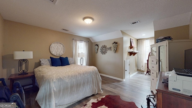 bedroom with a textured ceiling, vaulted ceiling, and hardwood / wood-style flooring