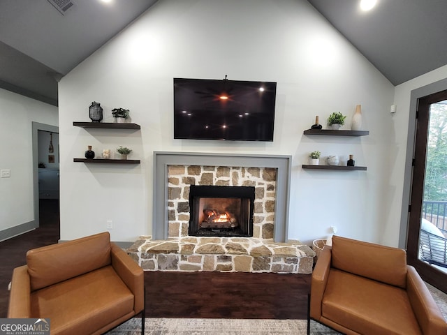 living room with vaulted ceiling, hardwood / wood-style flooring, and a stone fireplace