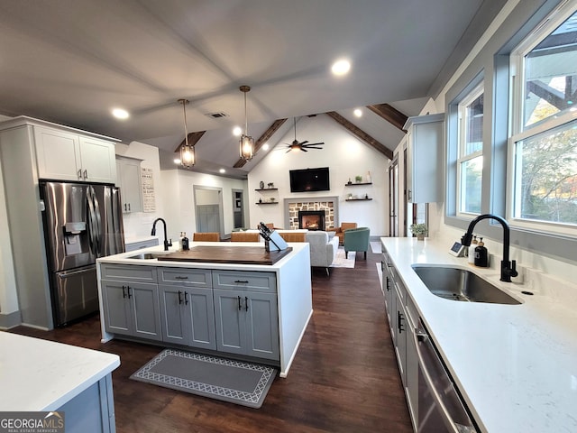 kitchen with lofted ceiling with beams, a stone fireplace, sink, decorative light fixtures, and stainless steel appliances