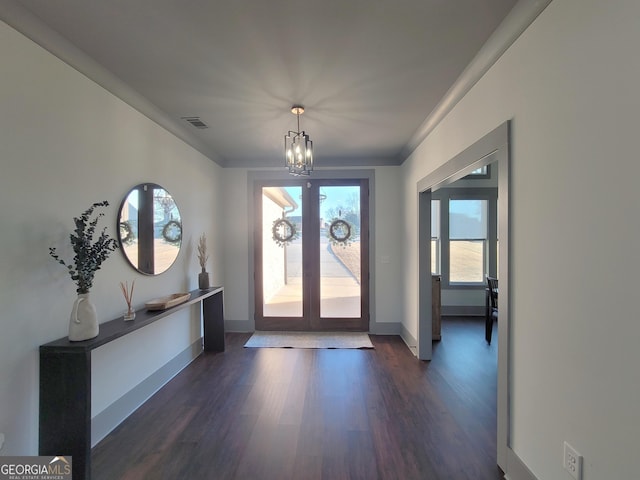 foyer with french doors, dark wood-type flooring, an inviting chandelier, and crown molding