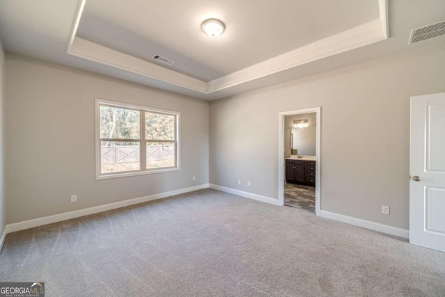 unfurnished bedroom featuring a raised ceiling, connected bathroom, and light carpet