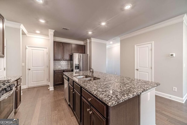 kitchen with sink, light hardwood / wood-style flooring, decorative backsplash, an island with sink, and appliances with stainless steel finishes