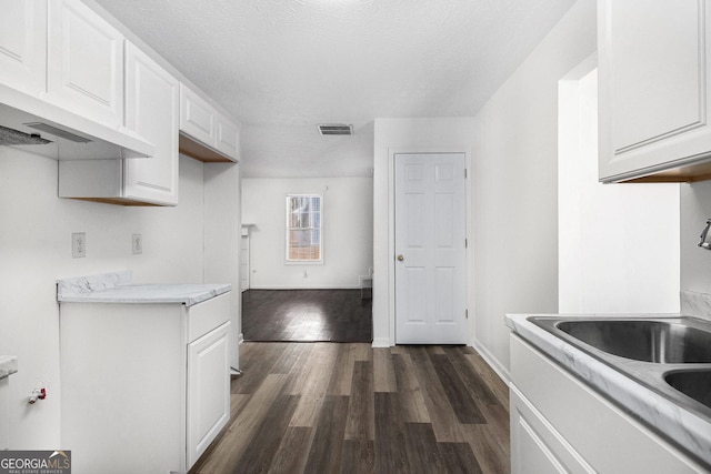 kitchen with dark hardwood / wood-style floors, white cabinetry, sink, exhaust hood, and a textured ceiling