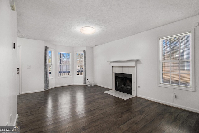 unfurnished living room featuring a tiled fireplace, dark hardwood / wood-style floors, and a textured ceiling