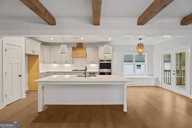 kitchen with french doors, sink, decorative light fixtures, a center island with sink, and white cabinets