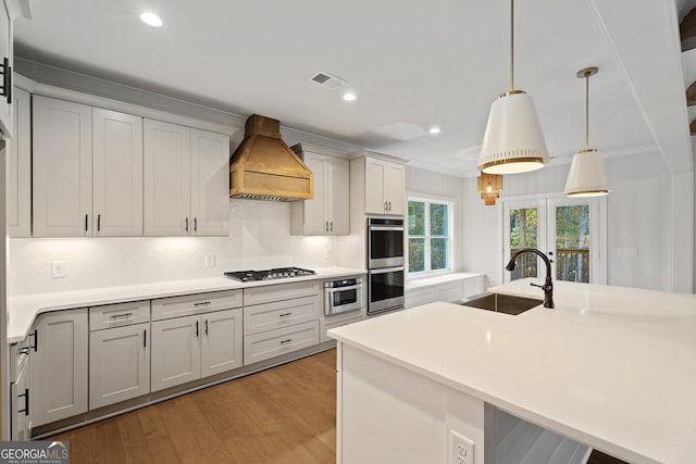 kitchen featuring appliances with stainless steel finishes, backsplash, custom range hood, sink, and pendant lighting