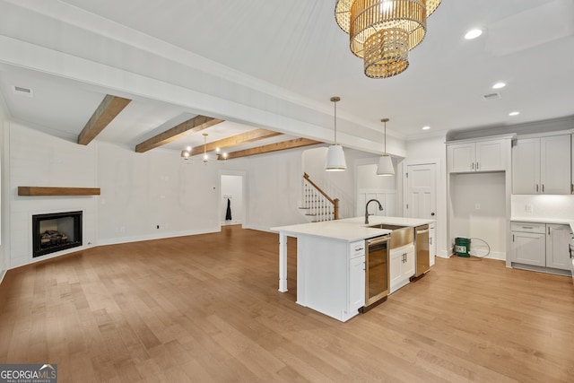 kitchen featuring beamed ceiling, white cabinets, a center island with sink, and hanging light fixtures