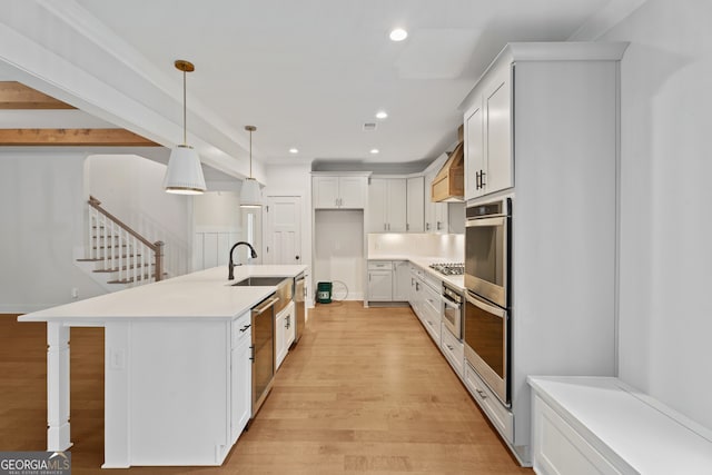 kitchen with sink, stainless steel appliances, an island with sink, decorative light fixtures, and white cabinets