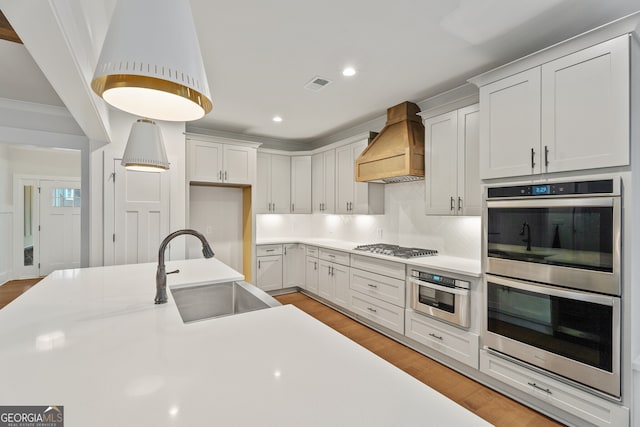 kitchen featuring custom range hood, stainless steel appliances, white cabinetry, and sink