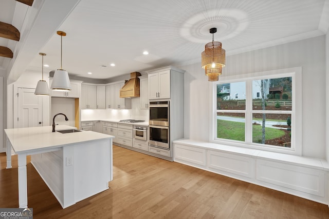 kitchen with premium range hood, sink, stainless steel appliances, and decorative light fixtures