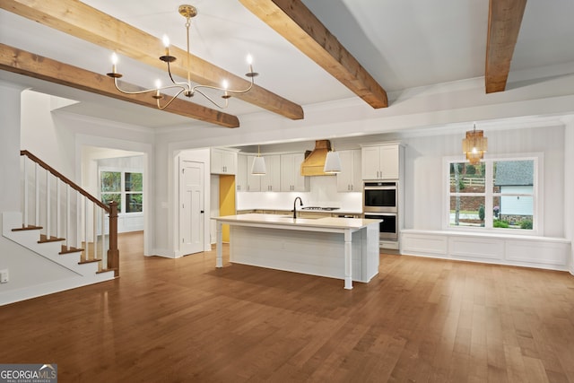 kitchen with a center island with sink, decorative light fixtures, white cabinetry, and premium range hood