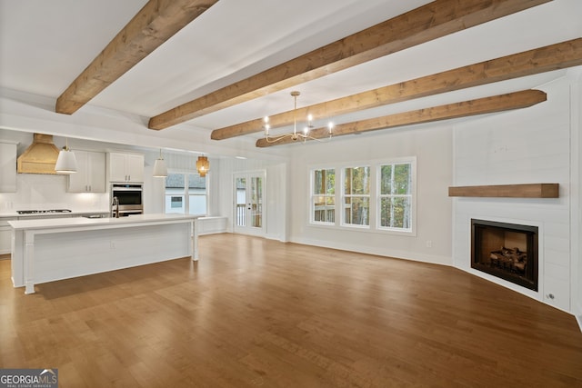 unfurnished living room featuring beam ceiling, light hardwood / wood-style floors, an inviting chandelier, and sink