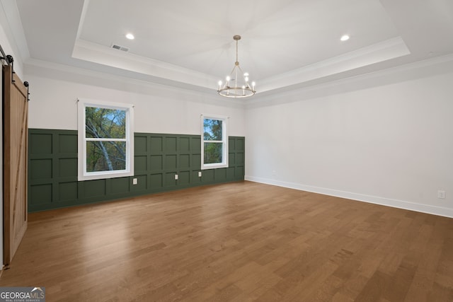 unfurnished room with a barn door, a tray ceiling, hardwood / wood-style flooring, and a notable chandelier