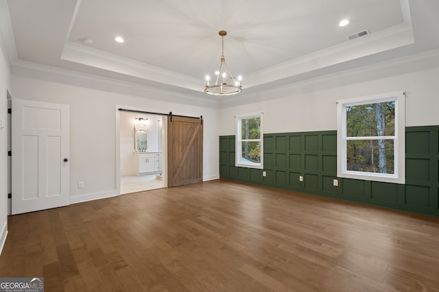 unfurnished bedroom with a barn door, a tray ceiling, an inviting chandelier, and hardwood / wood-style flooring