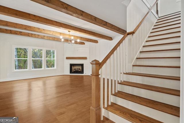 staircase with beamed ceiling, wood-type flooring, and a notable chandelier