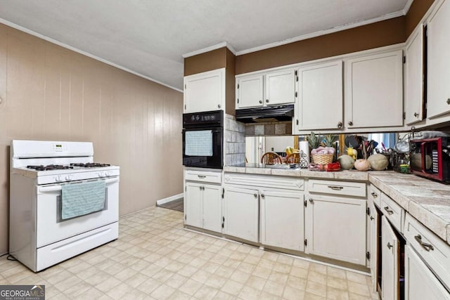 kitchen with ornamental molding, wooden walls, black appliances, white cabinets, and tile counters