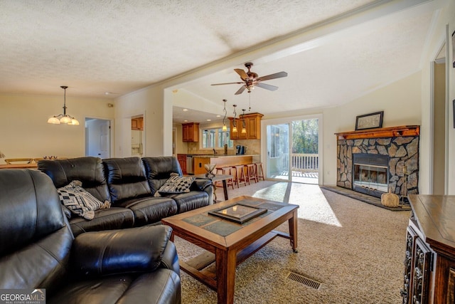 living room featuring carpet flooring, a stone fireplace, ceiling fan with notable chandelier, and a textured ceiling