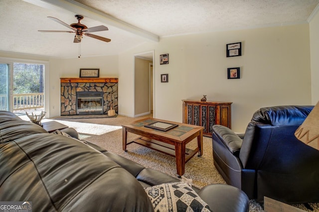 living room with ceiling fan, a stone fireplace, beamed ceiling, carpet floors, and a textured ceiling